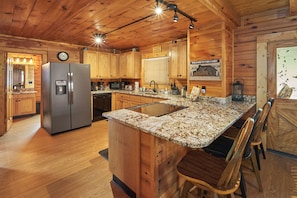 Een keuken in chaletstijl met houten kasten, een roestvrijstalen koelkast, een granieten aanrechtblad en een inbouwkookeiland met barstoelen.