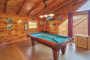 A wooden pool table in a cabin with wooden walls, a clock, and a window with blinds. - Pool Table | Pigeon Forge | Hot tub | Fireplace | Arcade | WiFi (Pigeon Forge)