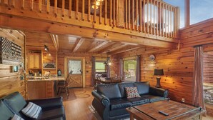 A cozy cabin interior with a wooden dining area, a black leather sofa, and a wooden coffee table. - Pool Table | Pigeon Forge | Hot tub | Fireplace | Arcade | WiFi (Pigeon Forge)