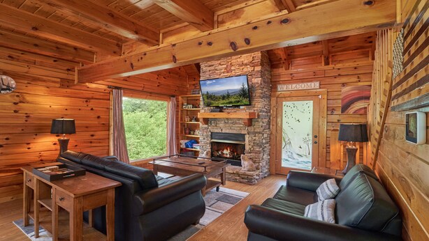 A cozy cabin interior with a stone fireplace, a television mounted on the wall, and a comfortable seating area with a sofa and a coffee table. - Pool Table | Pigeon Forge | Hot tub | Fireplace | Arcade | WiFi (Pigeon Forge)