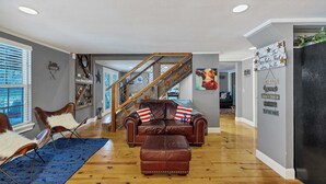 A spacious living room with a leather sofa, a blue rug, and a wooden staircase. - Roz's Rusted Porch - Whitewater Amp, River, Lake (Canyon Lake)