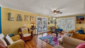 A living room with a yellow wall, a ceiling fan, and a large window with blinds. - Roz's Rusted Porch - Whitewater Amp, River, Lake (Canyon Lake)
