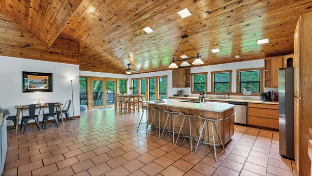 A spacious kitchen with wooden cabinets, a large island with bar stools, and a view of the outdoors through large windows.