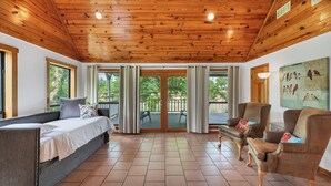 A room with a wooden ceiling, a bed, a sofa, a chair, and a painting on the wall.