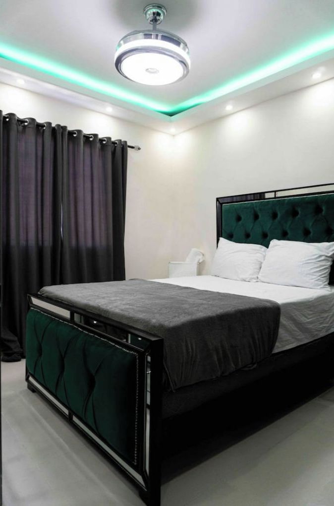 Un dormitorio moderno con una cama tapizada en verde, ropa de cama blanca y una lámpara de techo.