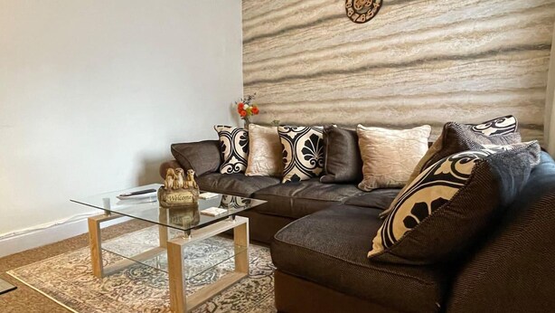 A living room with a sofa, patterned cushions, a glass coffee table, and a decorative wall piece. - Impeccable 4-bed Home Away From Home in Swindon (Swindon)