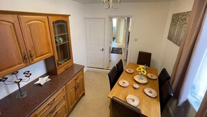 A dining area with a wooden table set for four, a cabinet with glass doors, and a chandelier. - Impeccable 4-bed Home Away From Home in Swindon (Swindon)