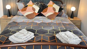 A neatly made bed with a geometric patterned bedspread, two decorative pillows, and two bedside lamps. - Impeccable 4-bed Home Away From Home in Swindon (Swindon)