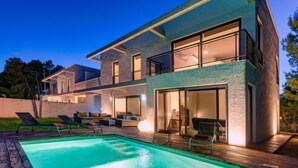 Una casa moderna de dos pisos con piscina, mobiliario exterior y ventanas amplias.