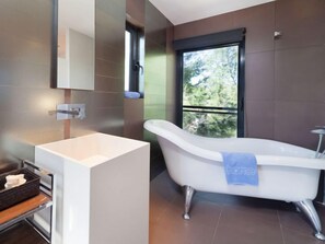 A modern bathroom with a freestanding bathtub, a large mirror, and a window providing a view of greenery. - Villa Luxor by Interhome (L'Ametlla de Mar)