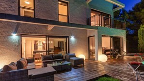 Una casa moderna de dos pisos con terraza, mobiliario exterior y ventanas amplias.
