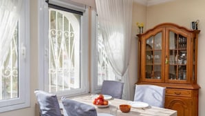 A dining area with a table set for two, a wooden cabinet with glass doors, and a window with curtains. - Villa Resi by Interhome (Miami Platja)