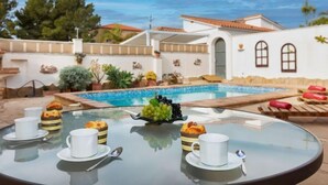 A poolside dining area with a glass table, white cups, and pastries. - Villa Resi by Interhome (Miami Platja)