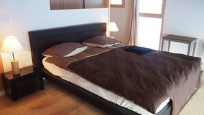 Ein ordentlich bezogenes Bett mit dunklem Kopfteil, zwei Nachttischlampen und einem Fenster mit Vorhängen.