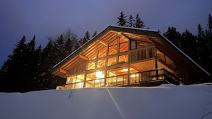 Eine Hütte mit großer Glasscheibe, umgeben von Schnee und Bäumen.