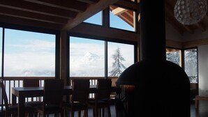 Ein Zimmer mit großen Fenstern, einem Essbereich mit Stühlen und einem großen, dunklen, runden Objekt im Vordergrund.