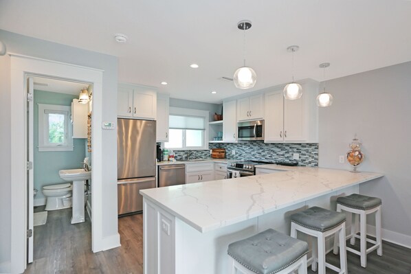 A modern kitchen with white cabinets, stainless steel appliances, and a marble island with bar stools.