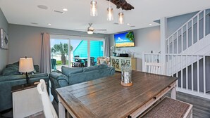 A spacious living room with a wooden dining table, teal sofas, and a large TV.