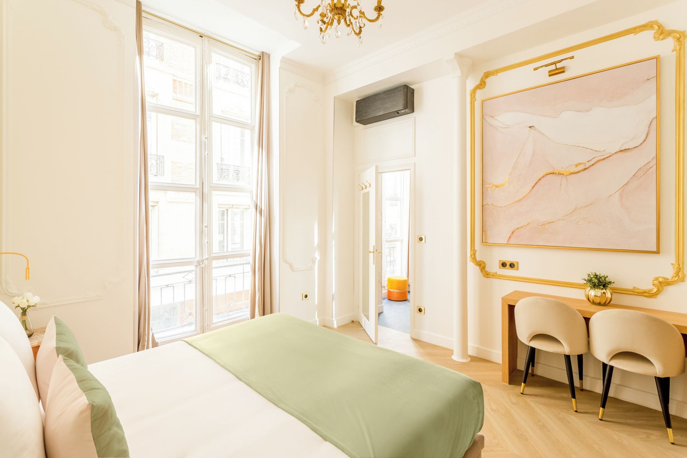 A hotel room with a bed, a desk with two chairs, a large abstract painting, and a view of the outside.