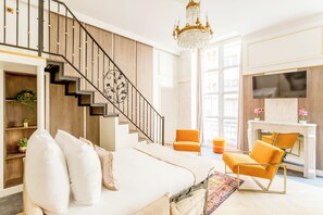 A modern living room with a staircase, a sofa, an orange armchair, and a fireplace.