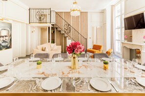 A spacious dining area with a marble table set for a meal, a staircase leading to an upper level, and a television mounted on the wall.