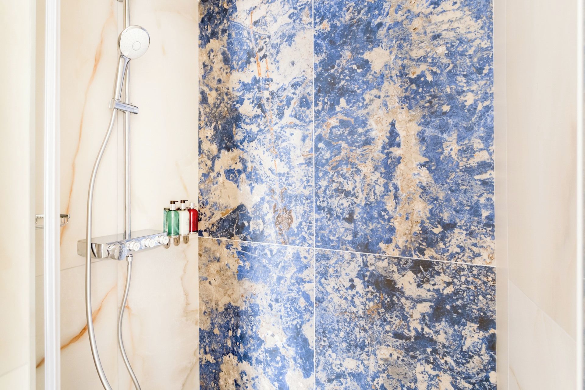Un baño con ducha, secamanos y estante con artículos de aseo.