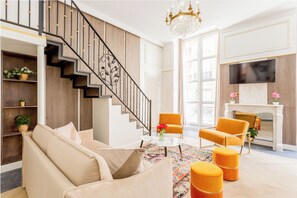A modern living room with a staircase, a sofa, ottomans, a coffee table, and a fireplace.
