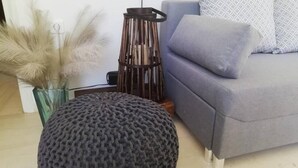 Sala de estar con sofá gris, cojines estampados, un taburete redondo de punto, una lámpara de pie alta y un jarrón con plantas secas.