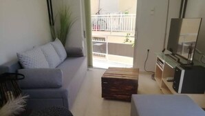 Una sala de estar con un sofá gris, una mesa de centro de madera, un taburete redondo y un televisor sobre un mueble de madera.