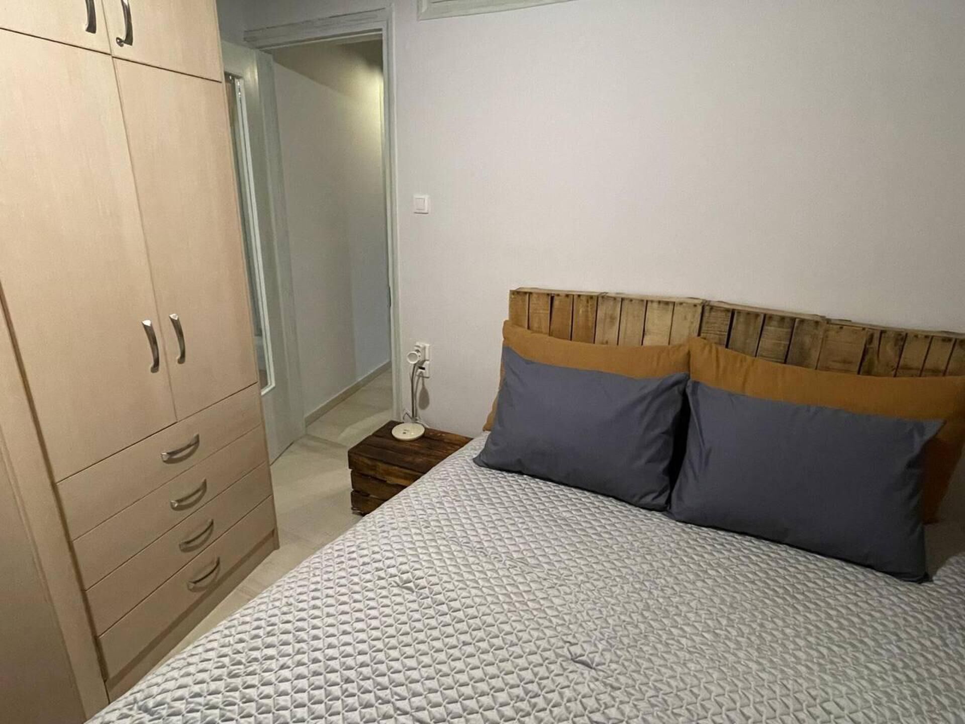 A bedroom with a bed, wooden wardrobe, and a bedside table.