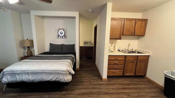 Ein Schlafzimmer mit Bett, Deckenventilator und einer Küchenzeile mit Holzausstattung und Spüle.
