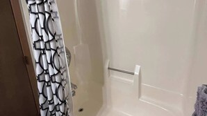 Eine Duschkabine mit Glastüren, eine weiße Badewanne, ein Handtuchhalter und ein gemustertes Vorhang.