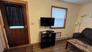 Ein Wohnzimmer mit Holztür, einer schwarzen Unterhaltungseinheit mit Fernseher, einem schwarzen Sofa und einem gemusterten Teppich.