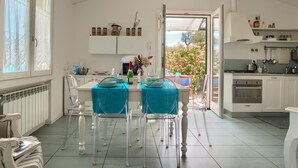 Una cuina luminosa amb armaris blancs, una zona de menjador amb taula i caires, i vista a l'exterior.