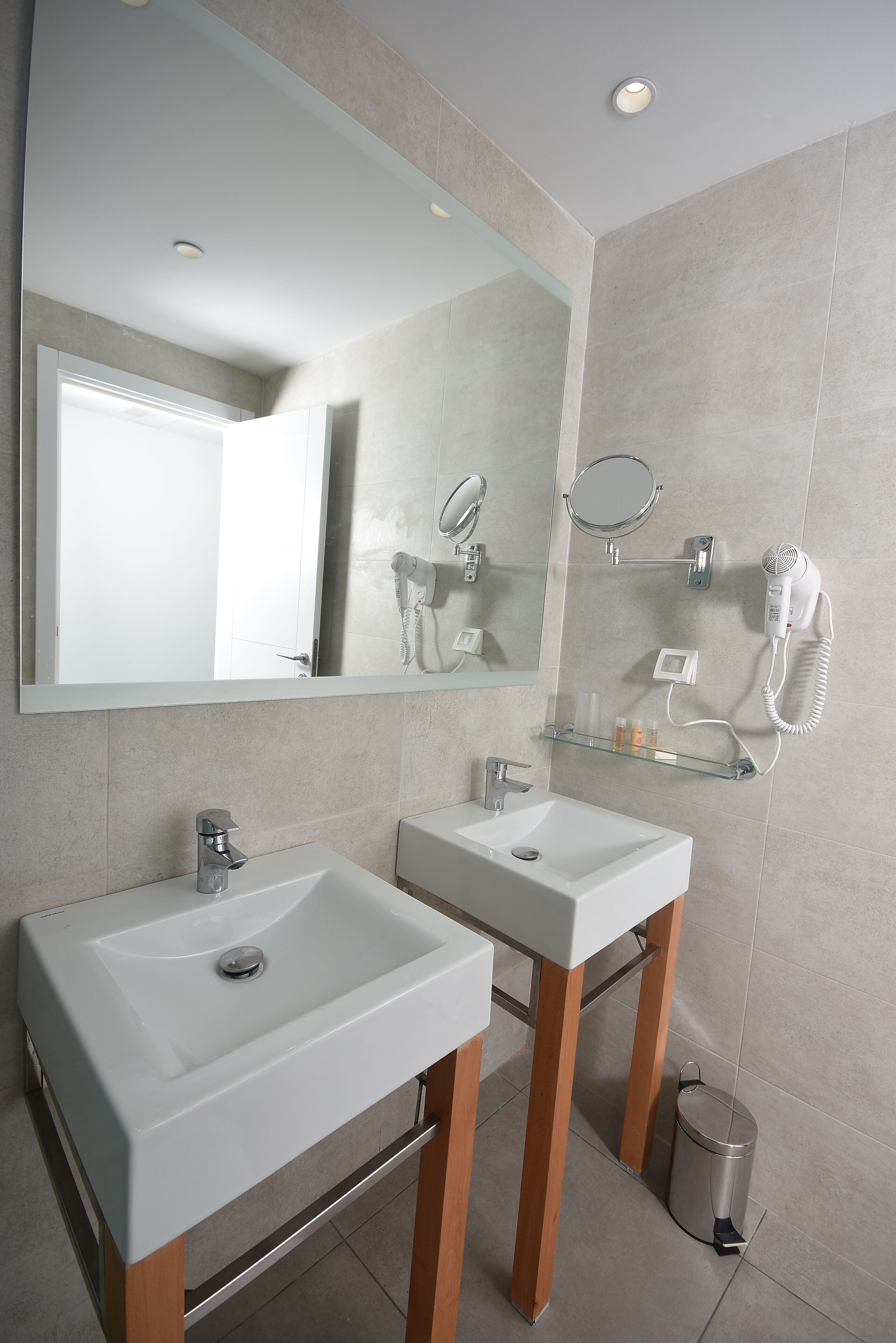 Une salle de bain moderne avec deux lavabos, un grand miroir, un sèche-cheveux et une poubelle.