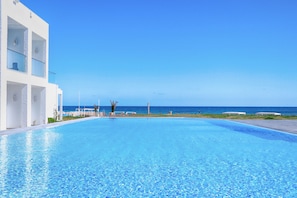 A swimming pool with a view of the ocean and a white building with balconies.