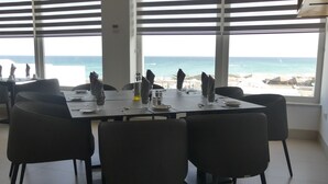 A dining area with a table set for four, large windows with a view of the sea, and modern chairs. - Amber El Fell- Boutique Hotel (Hammamet)
