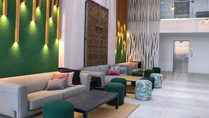 A modern lobby with a grey sofa, green ottomans, and a large decorative wall. - Amber El Fell- Boutique Hotel (Hammamet)