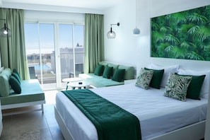 A hotel room with a balcony, a bed with green bedding, a sofa, and a wall-mounted light fixture.