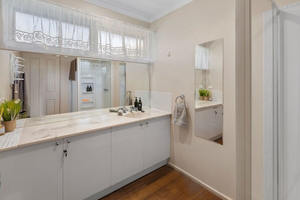 A modern bathroom with a large mirror, a sink, and a shower area. - Sunset Cove - Macs Cove (Macs Cove)