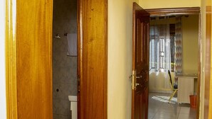 A hallway with wooden doors leading to a bathroom and a room with a desk and chair. - Comfort Apartment  (Kigali)