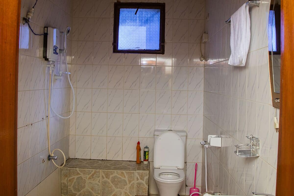 A bathroom with a toilet, sink, shower, and a small window.