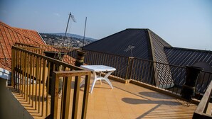 A rooftop terrace with a white table and chairs, a metal railing, and a view of a town in the background. - Comfort Apartment  (Kigali)