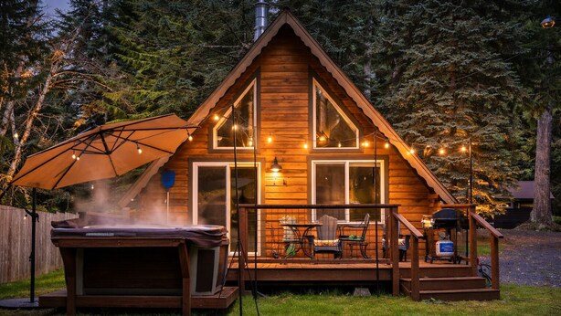 A wooden cabin with a deck, outdoor seating, and a hot tub.