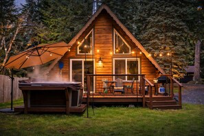 A wooden cabin with a deck, outdoor seating, and a hot tub.