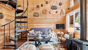 A cozy cabin interior with a spiral staircase, a sofa set, a fireplace, and hanging decorative lights.
