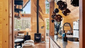 A cozy cabin interior with a wood-burning stove, a dining area, and a kitchen with a sink and refrigerator.