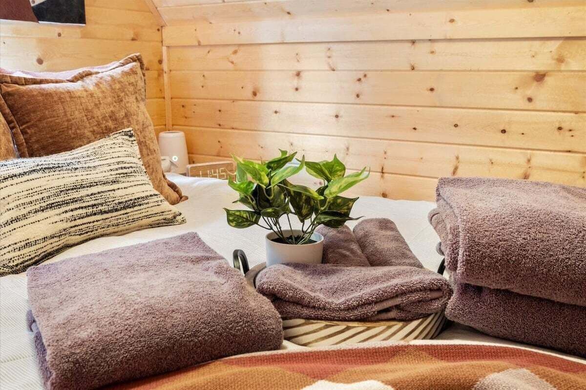 Una habitación estilo cabaña de madera con cama, almohadas, una planta en maceta y toallas dobladas.