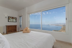 A bedroom with a large window, a bed, a dresser, and a mirror.