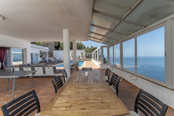 A covered outdoor dining area with a pool and a view of the sea.